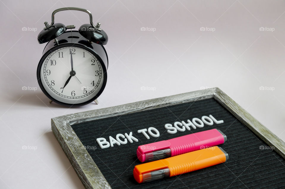 Felt board with message “Back to school” with colorful markers and alarm clock set to 7am on pastel background