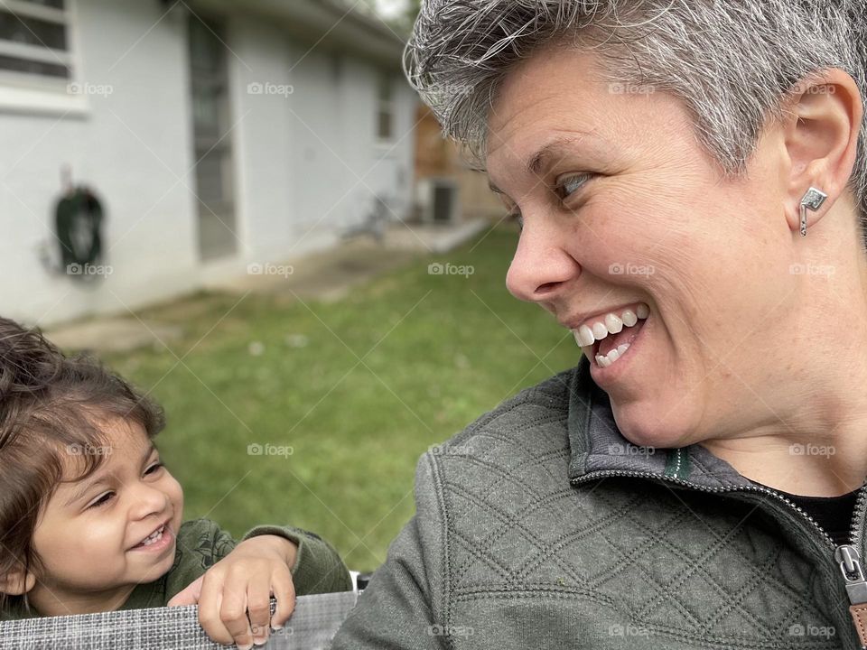 Toddler sneaks up on mother, cute toddler smiling with mother, mommy and toddler showing emotion of happiness, happy together, finding happiness in every moment, joking with a toddler, mother and toddler girl enjoy the backyard 