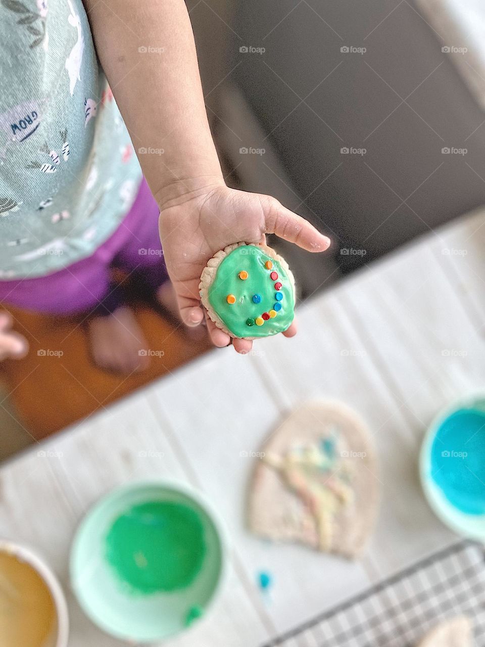 Toddler holding smiley face sugar cookie, toddler girl proud of her work, proud of her creation, showing off her sugar cookie, decorating sugar cookies, toddler uses icing and sprinkles to decorate sugar cookies, toddler hand holding a cookie