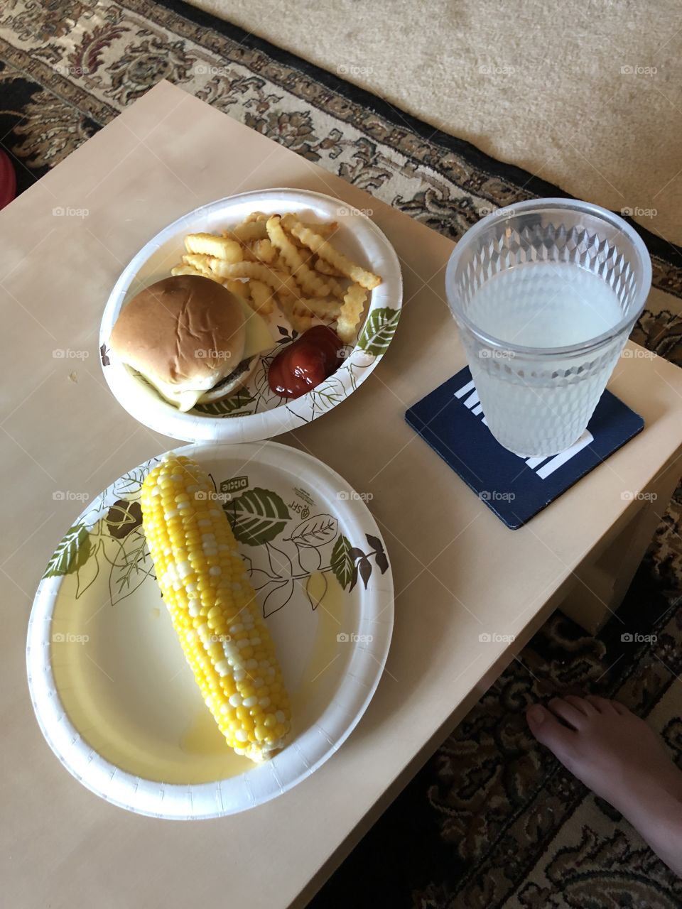 A summer feast on paper plates with lemonade, corn on the cob, a burger, French fries, and ketchup