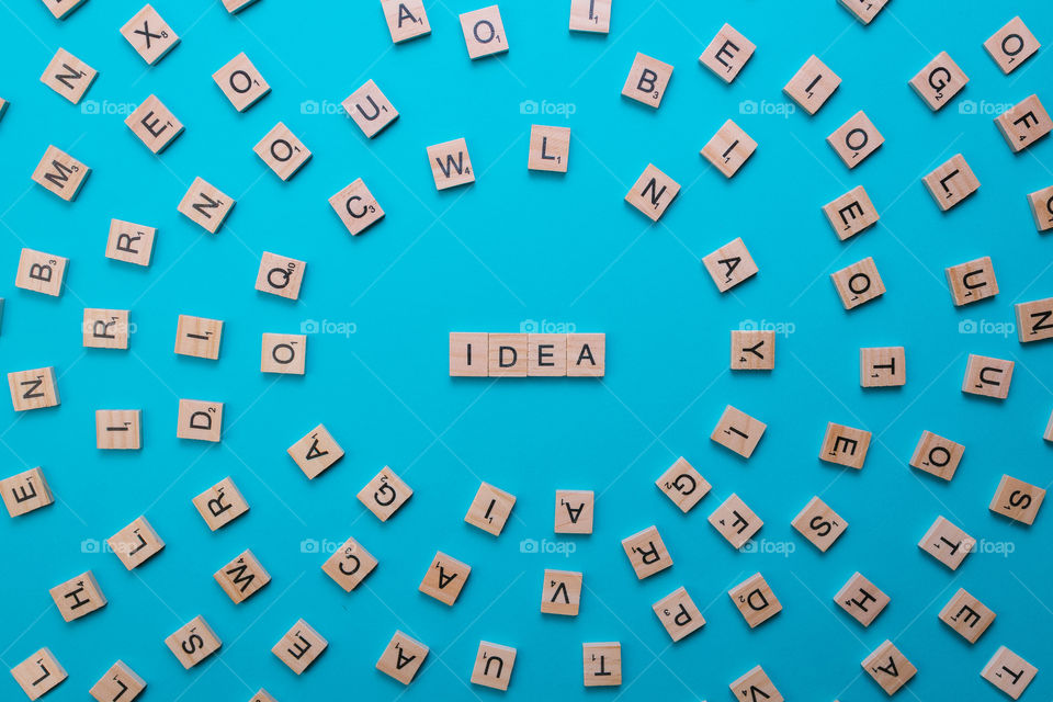 Word Idea formed by wooden letters in the composition center with all the letters of the alphabet on a light blue background. Top view