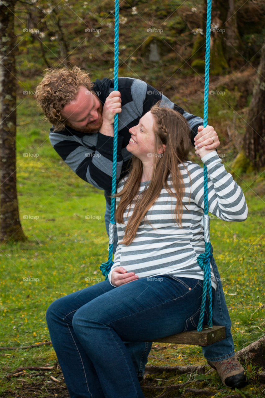Pregnant woman sitting in swing looking at her husband