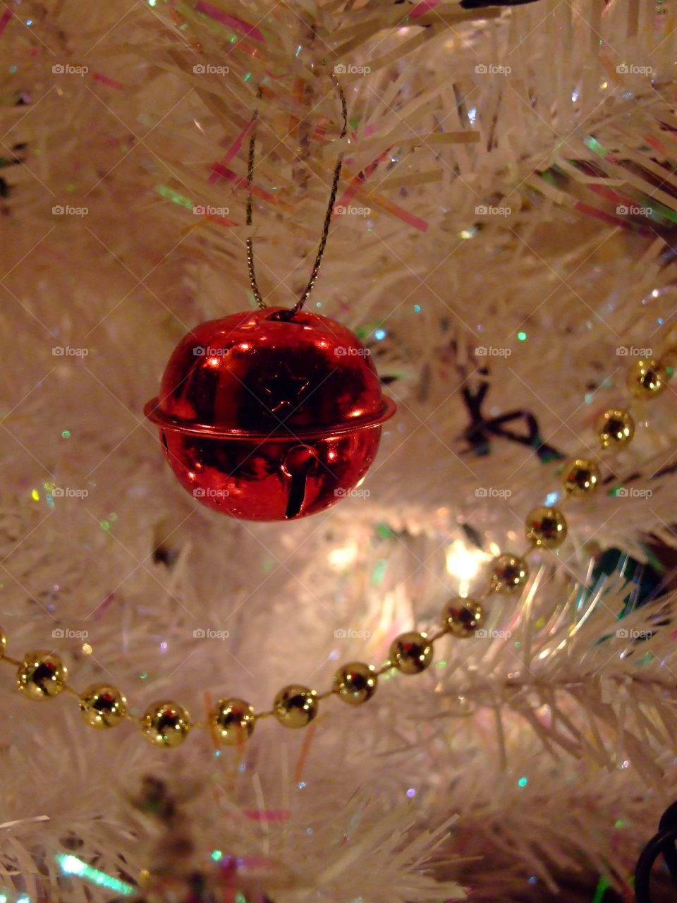 Red ornament on a glistening, white tree with round, gold beads
