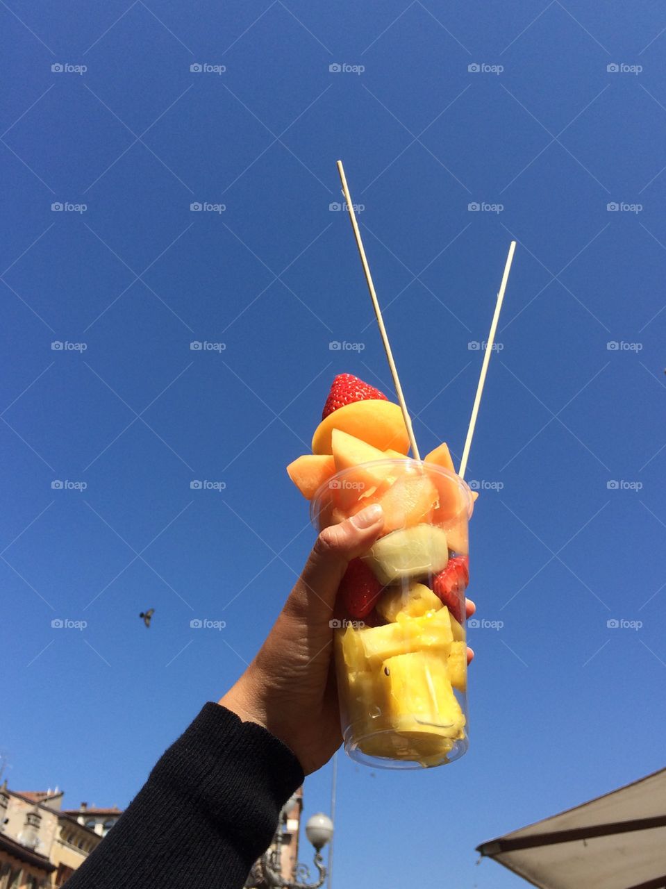 Hand holding fruits salad up to blue sky