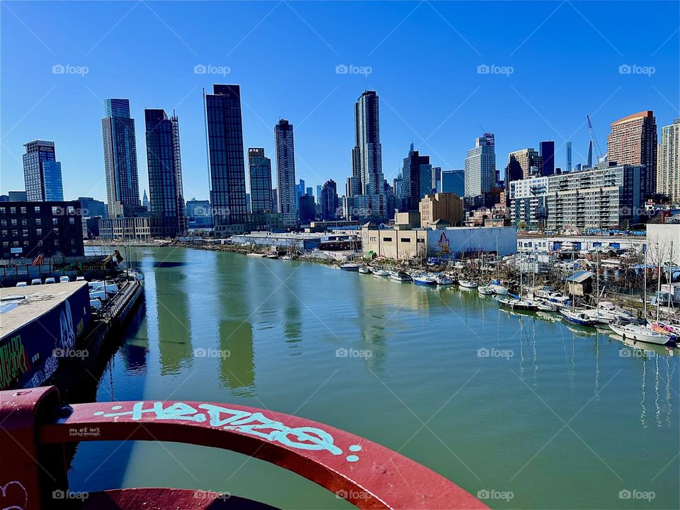 This is picturesque „Newtown Creek“ with all its beautiful boats seen from the „Pulaski Bridge“ that connects LIC, Queens to „Greenpoint“, Brooklyn. Across the water of the „East River“ behind LIC we see „Manhattan“. 2024. Hypnotic Productions