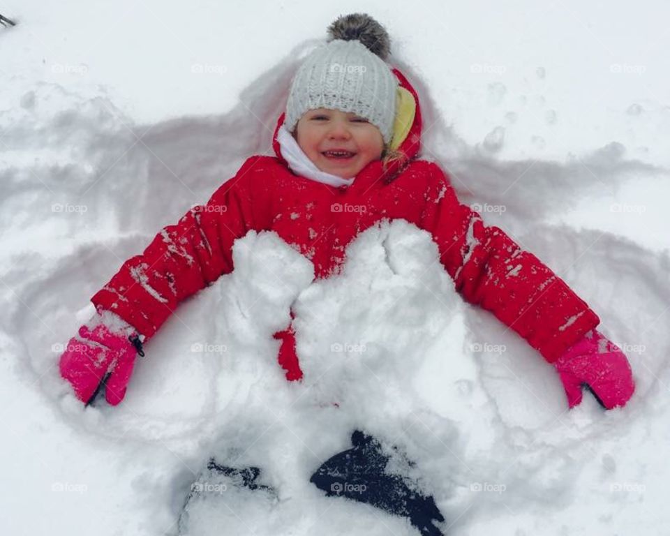 A child playing with snow making an angel