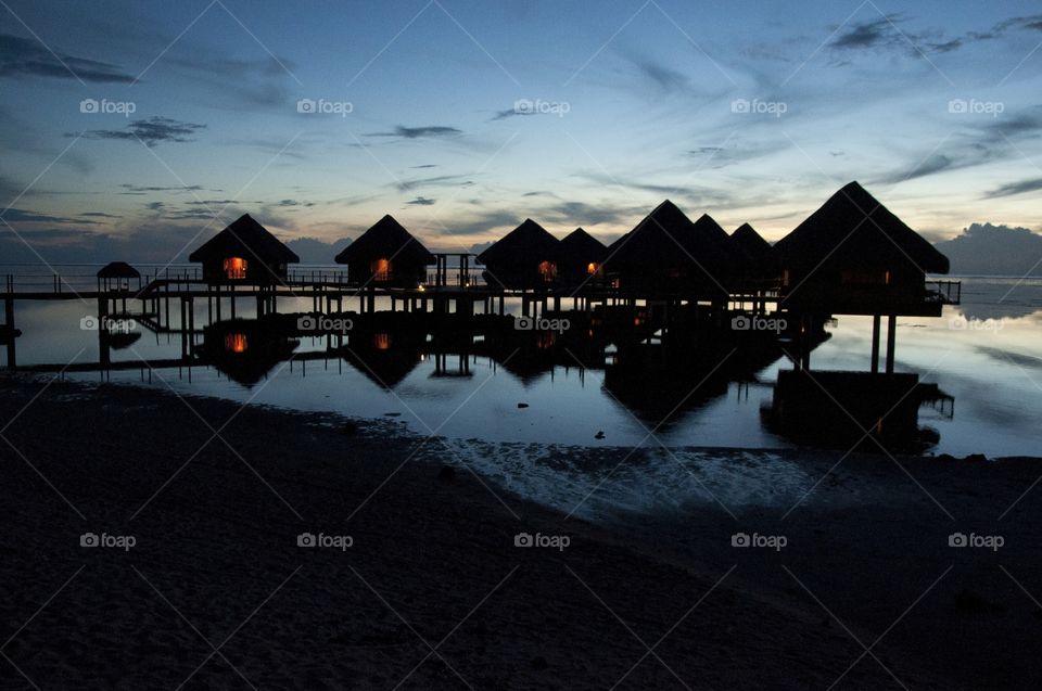 A silhouette is casts onto these bungelows amidst a Tahiti beach sunset.