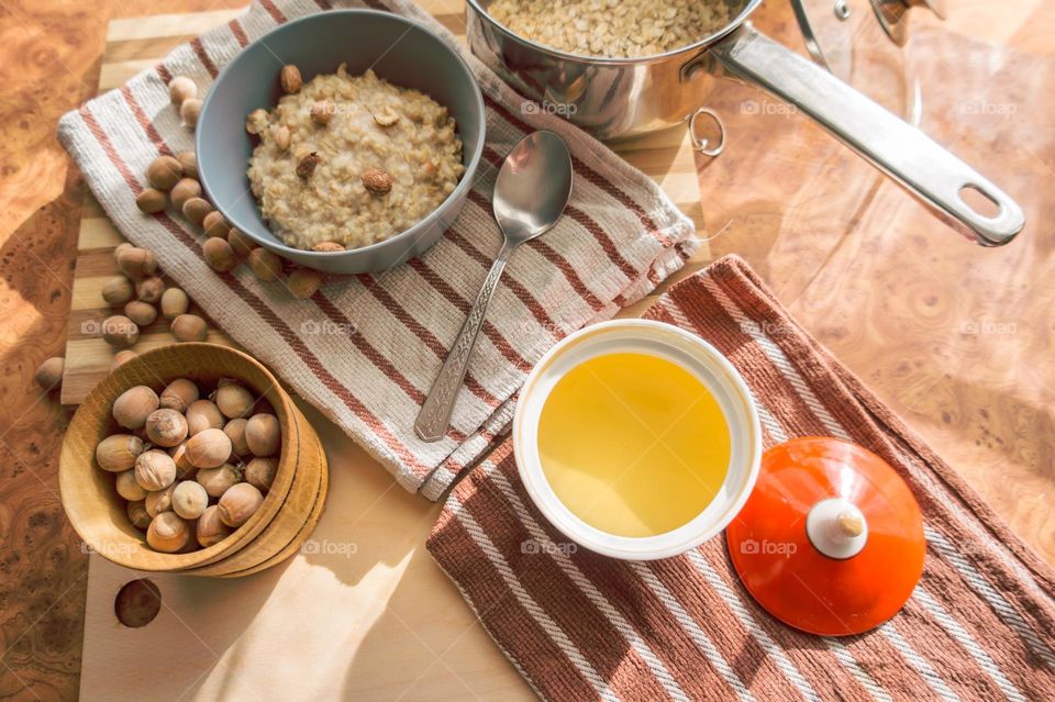 Cooked oatmeal in a deep gray plate with hazelnuts and honey.