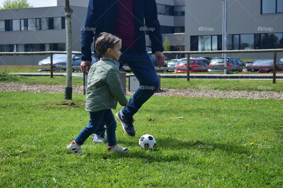 Little boy playing football with his father on the playground