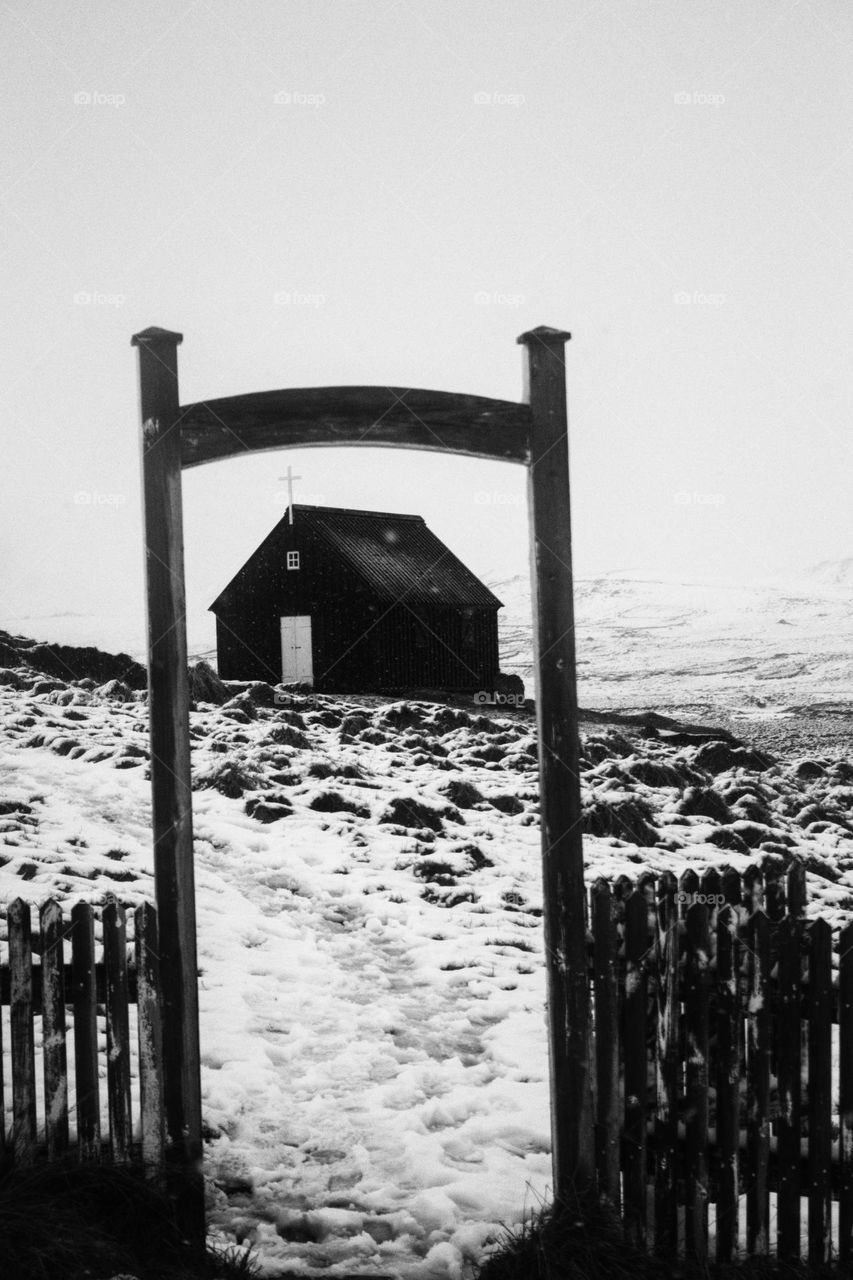 Black church in Iceland framed through the entrance door with footprints leading to the church.