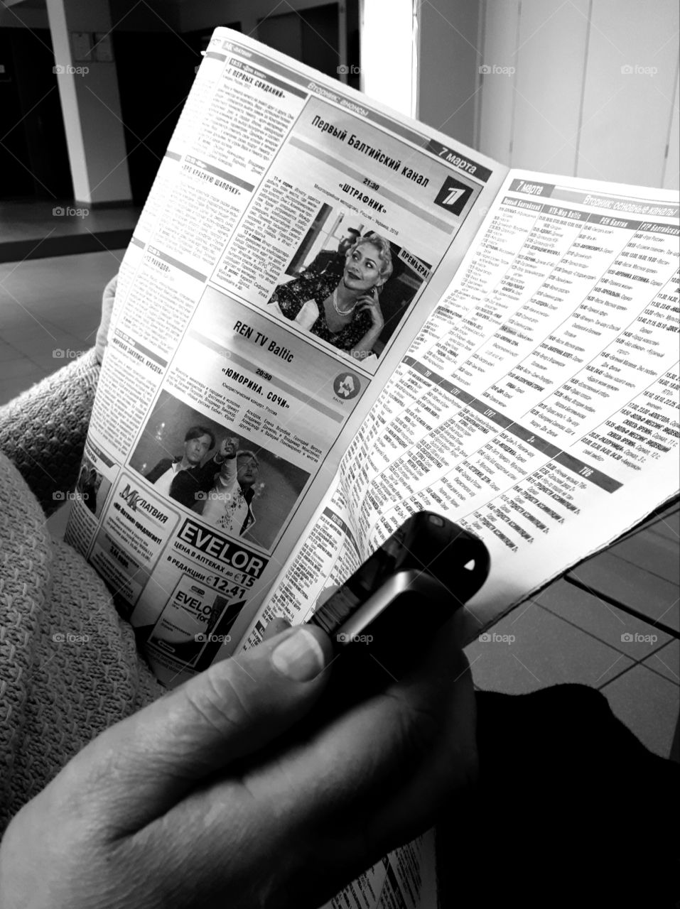 A woman reading newspaper and holding an old model smartphone in hand. Black and white photography.