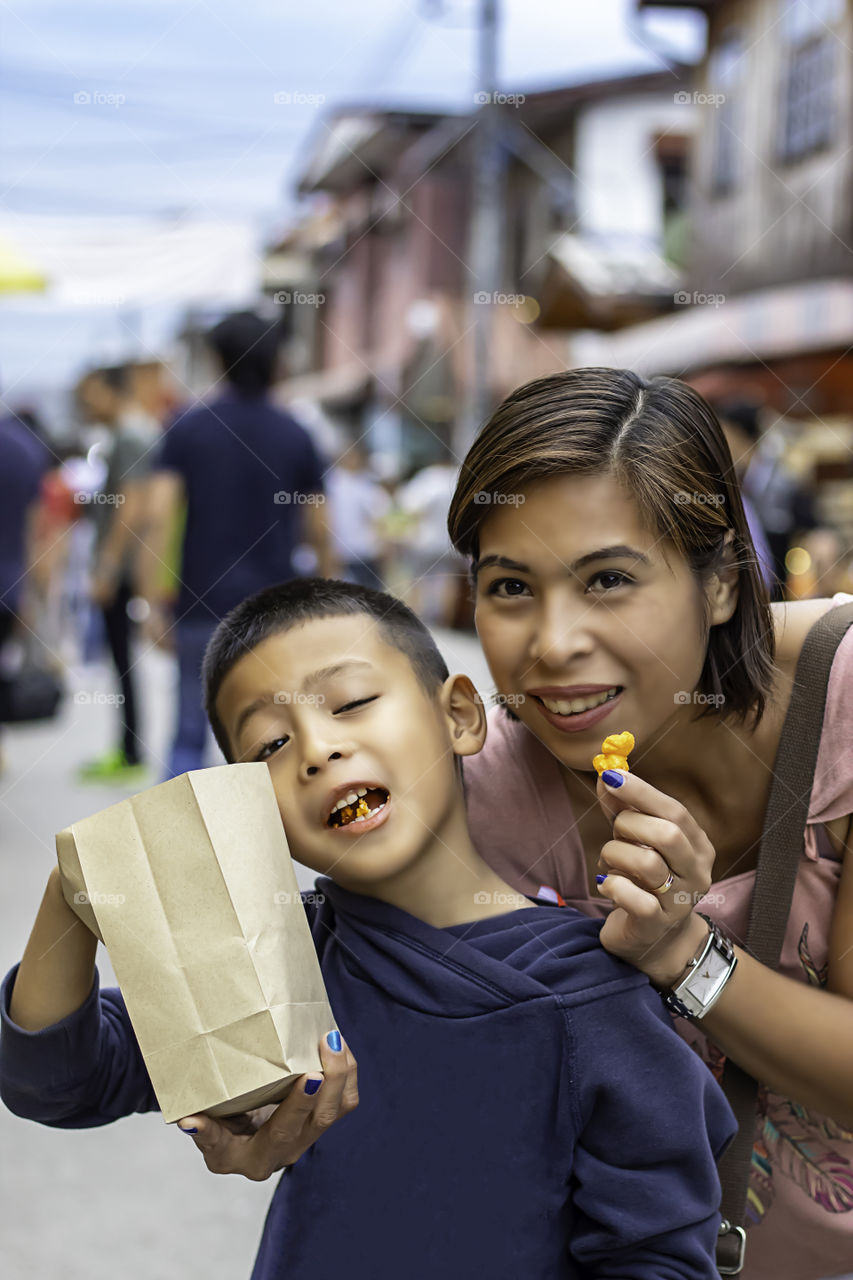 Mother and son eat candy on the street and blurry tourists at Walking Street Chiang Khan, Loei in Thailand.