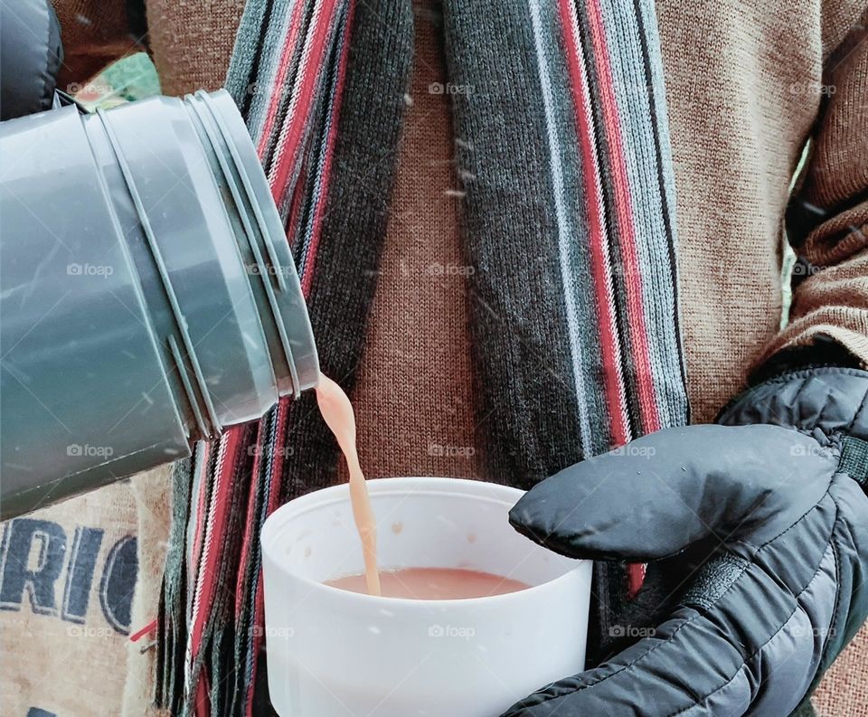 Hot tea poured from a flask by an outside worker on a cold & snowy day