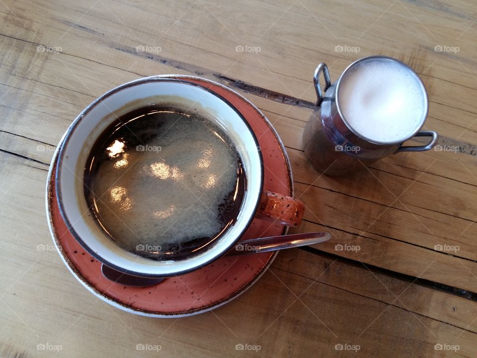 Black coffee in red orange cup with milk in mini milk can. coffee on wooden  table