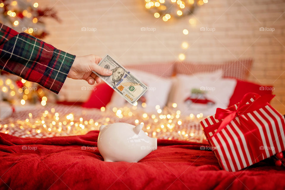 piggy bank with 100 dollars banknote in festive New Year atmosphere of scenery. Magical bokeh with Christmas tree and bright lights.