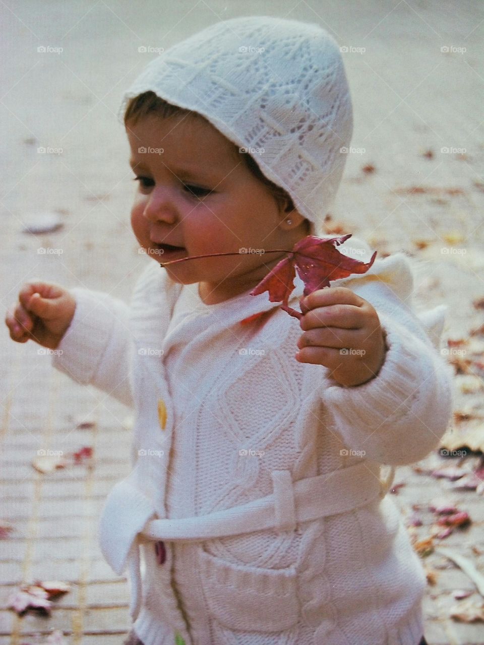 Baby in white warm clothing holding autumn leaf