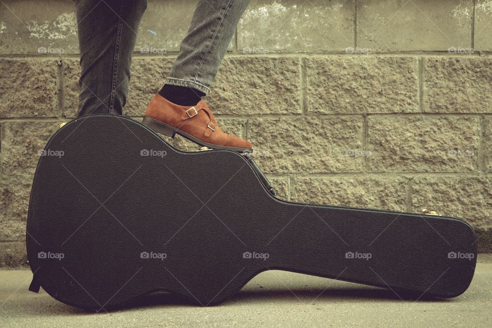 man put his foot on a hard guitar case. hard case for electric guitar. Man dressed in jeans holding guitar case against wall. guy with a guitar. copy space text