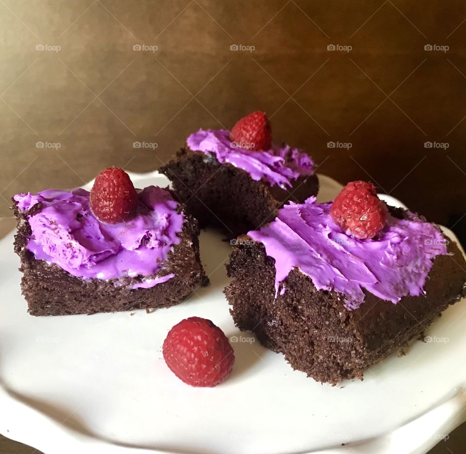 Sweet tooth craving - a delicious Serving of rich chocolate cake topped with bright purple creamy frosting with a yummy raspberry on top of each slice ! 3 slices of deep dark chocolate cake.