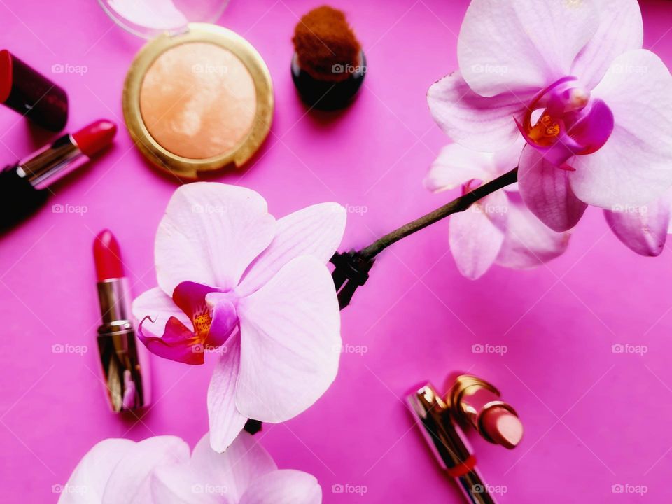 flat lay with lipsticks make up and an orchid on pink background