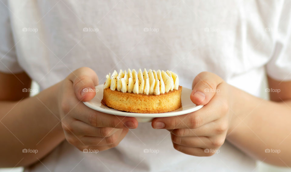 Sweet and delicious almond tart with vanilla cream on white plate in the hand of child.