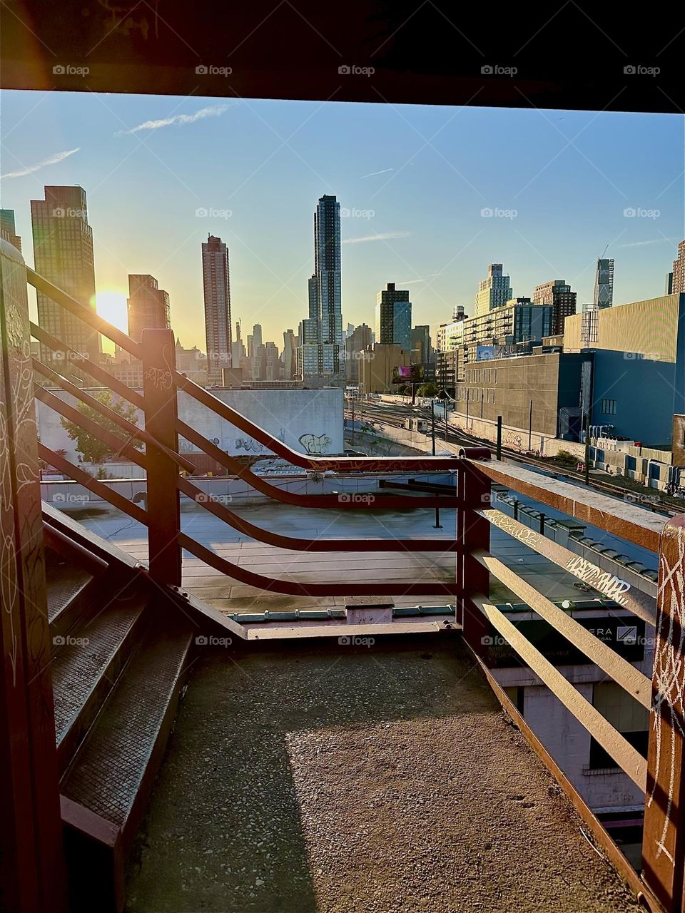 This is the red metal staircase of the “Pulaski Bridge” at “Newtown Creek” that connects “Greenpoint”, Bklyn to LIC, Queens overlooking the “Long Island Railroad” tracks and “iFly”, an indoor flight simulator. 2024. Hypnotic Productions