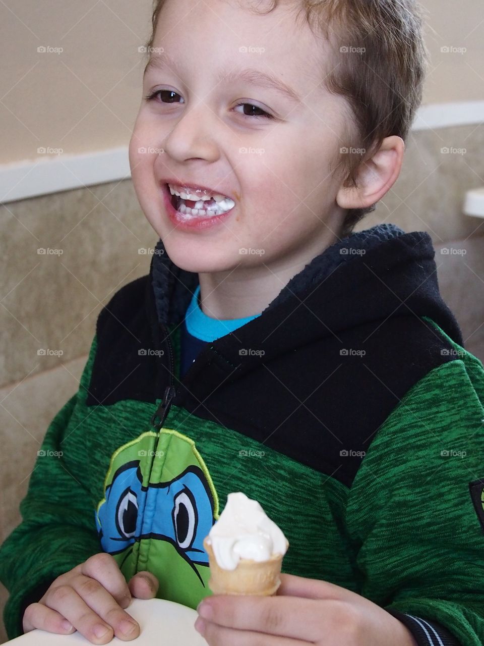 A little boy really enjoys his small vanilla cone that really hits the spot. 