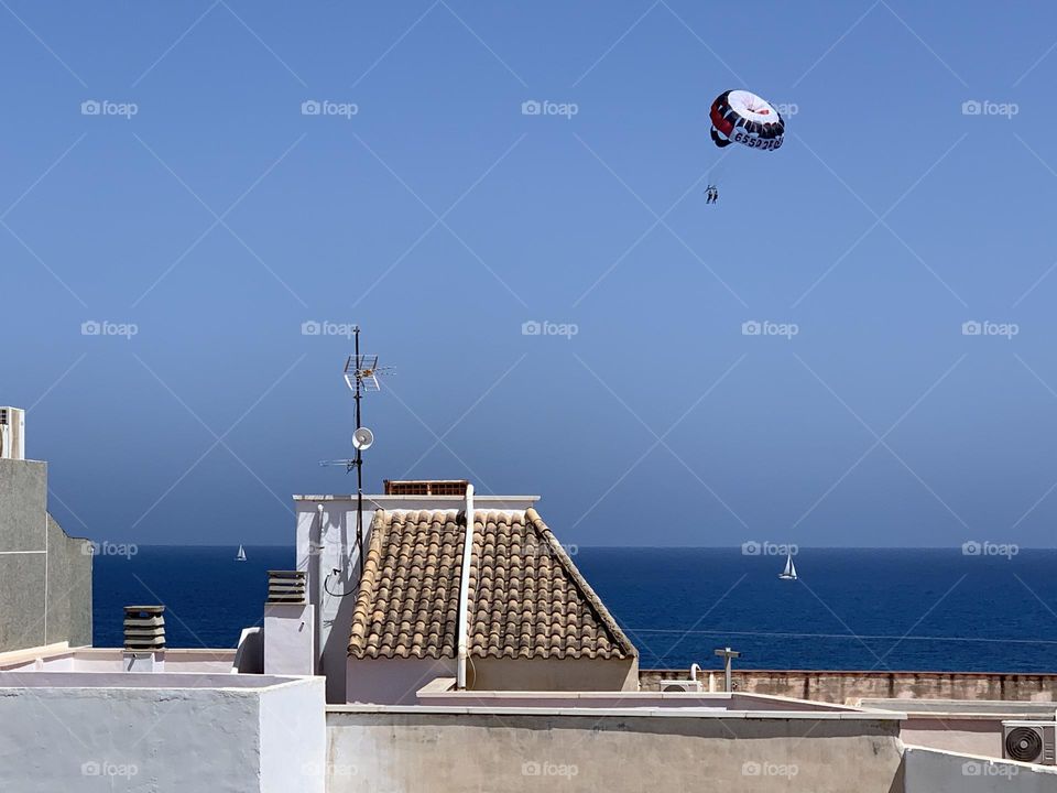 Paragliding with parachute above the sea, clear sky, white boats, front beach houses roofs