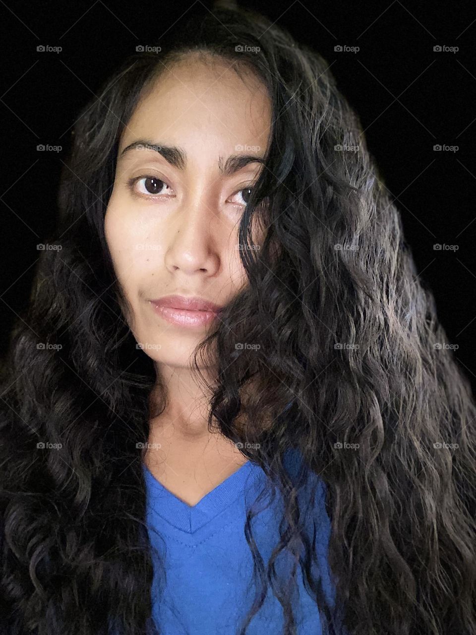 Selfie portrait of a woman with long black hair with black background. 