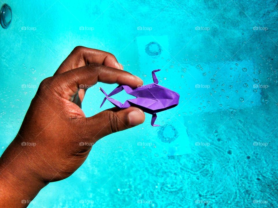 Purple origami frog in hand over the swimming pool