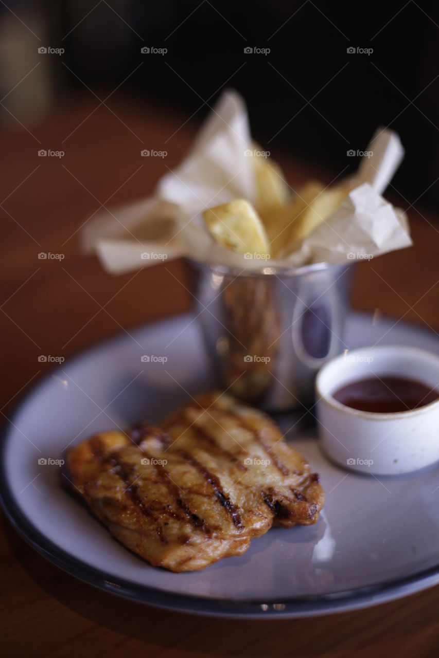 Delicious grilled chicken BBQ and french fries served on plate at a restaurant