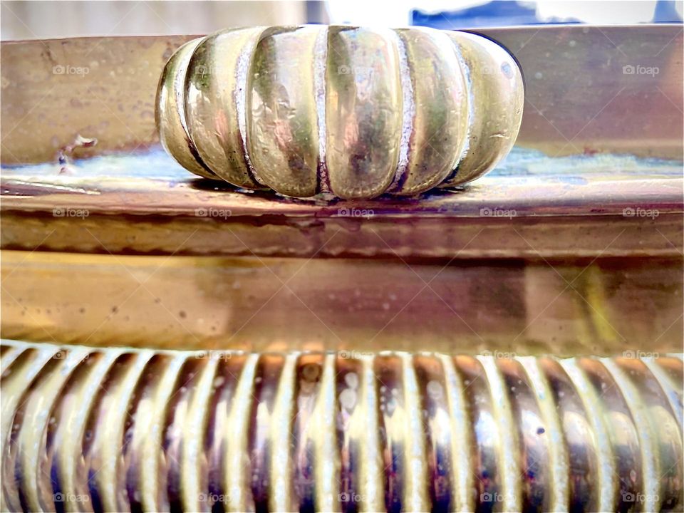 A closeup detail of the lavish bronze fireplace fender fit for palatial habitations, a rosetta inspired ornamented knob on top of one of the rounded corners. 2022. Hypnotic Productions