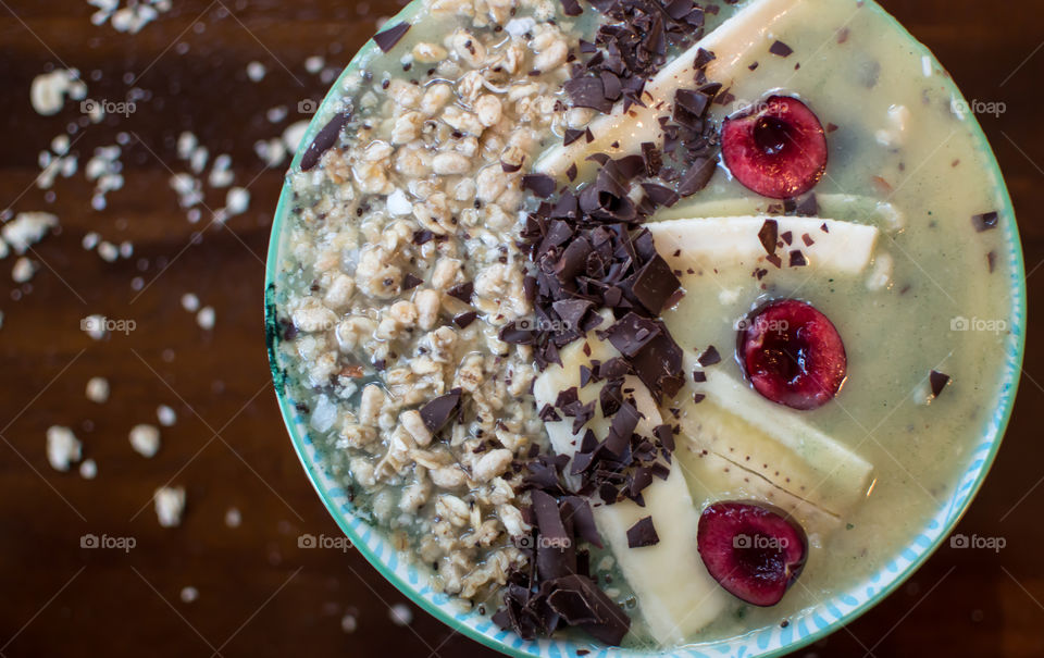 Chocolate banana and cherry with granola and coconut fresh fruit smoothie bowl decorated with sliced fruit from high angle view. Artisanal healthy eating food photography background