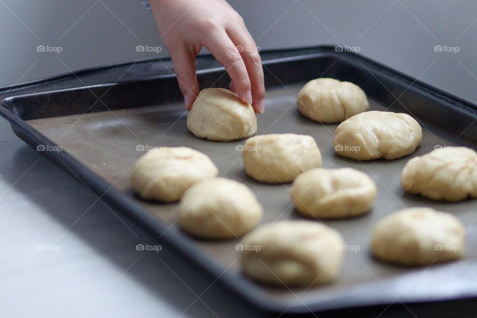 Child's hands are putting buns on a baking tray