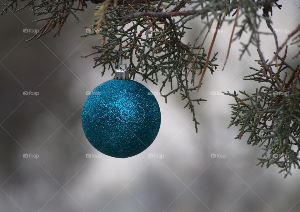 A glittering Christmas bulb hangs from a juniper tree on a cold day in a central oregon cemetary