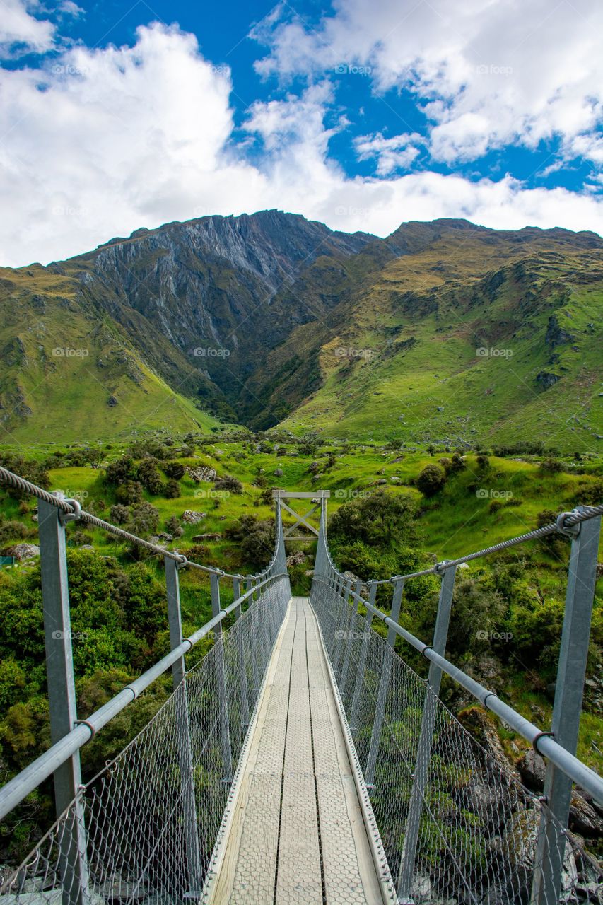 Puente colgante sobre los campos y la montaña de Nueva Zelanda