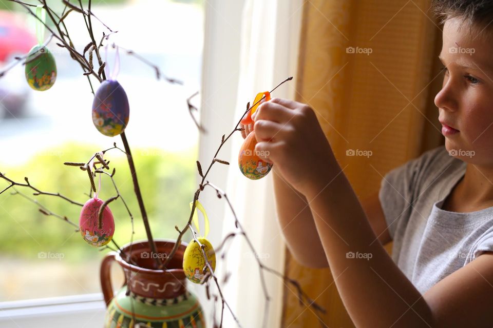 a boy of seven years old, paints crafts at home, Easter eggs, the boy is preparing for the holiday. home crafts, craft activity. a child decorates a tree branch with homemade eggs for Easter