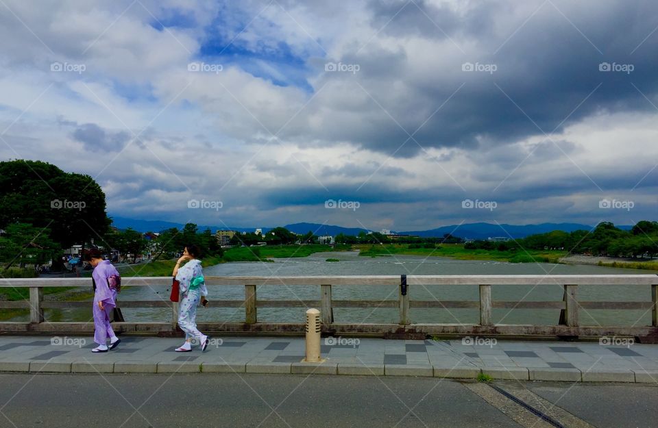 Two girls wear kimonos while walking across the Togetsukyo Bridge in Arashiyama Japan