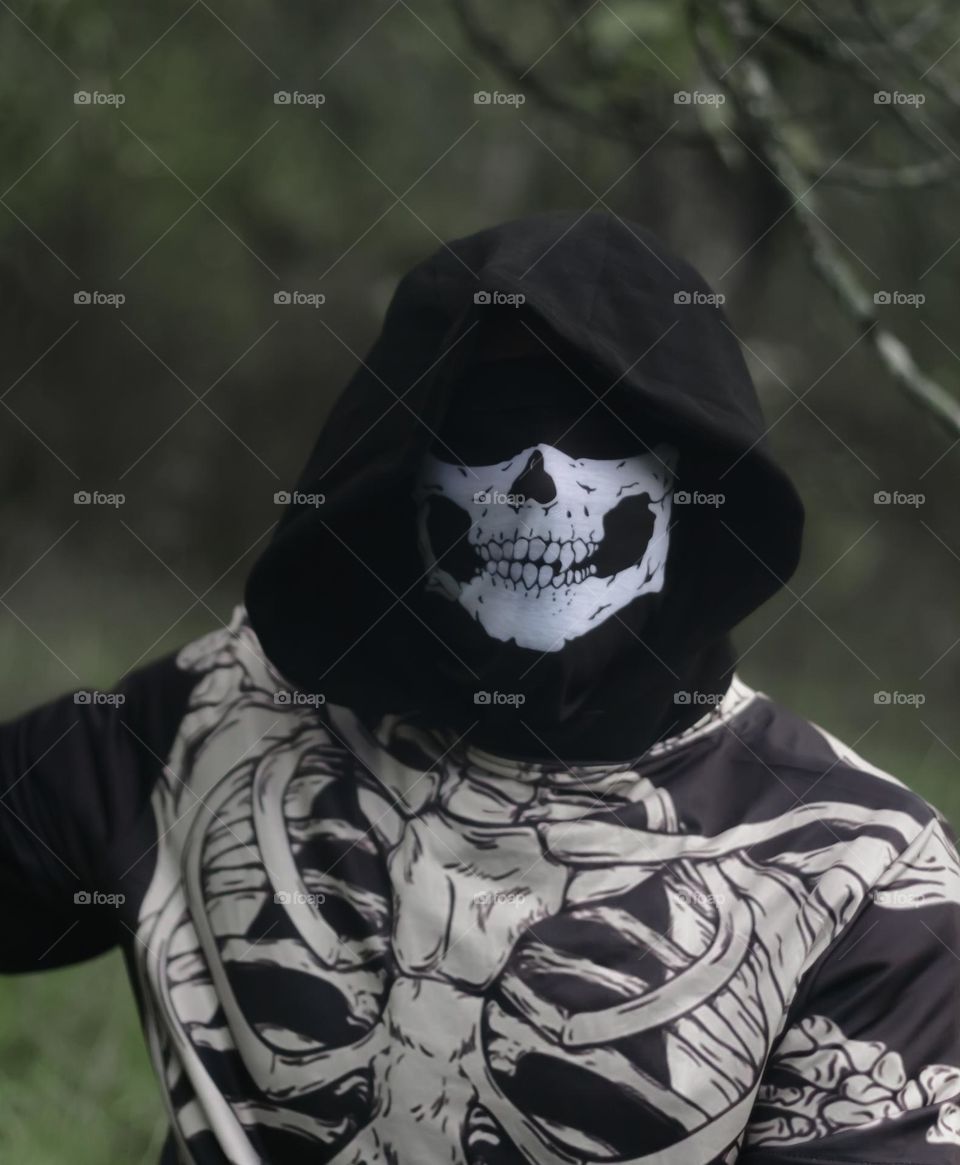 Man disguised in skeleton mask & t-shirt, with a hood pulled over his eyes