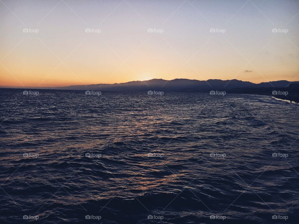 A peacefull picture of the ocean, the waves, the mountains, the sun/sunset. 