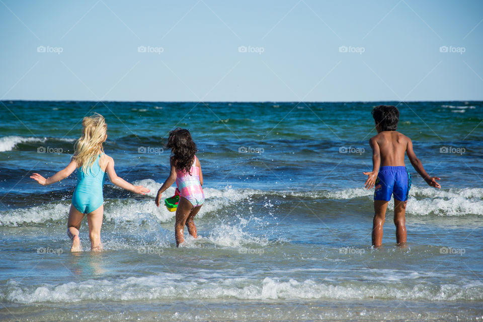 Young children jumping in the water at Höllviken beach in Sweden.