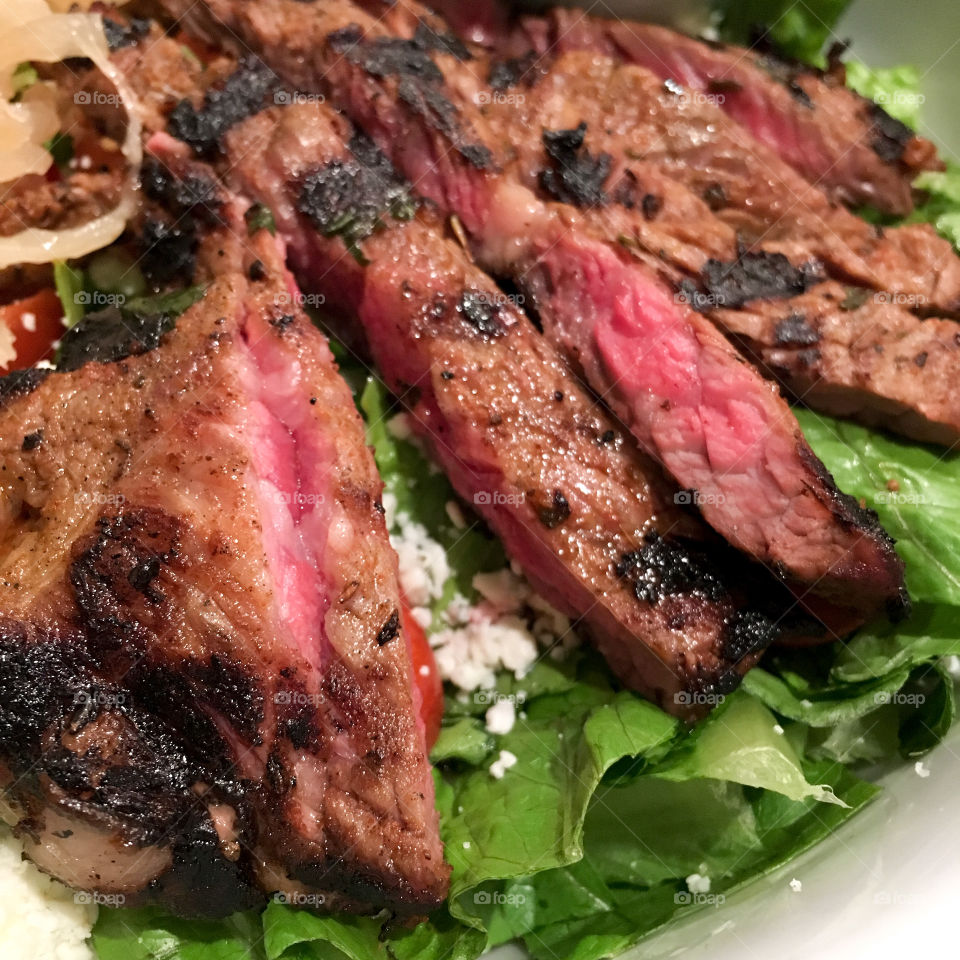 Square photo of steak salad, cooked medium rare on a bed of lettuce and blue cheese crumbles.