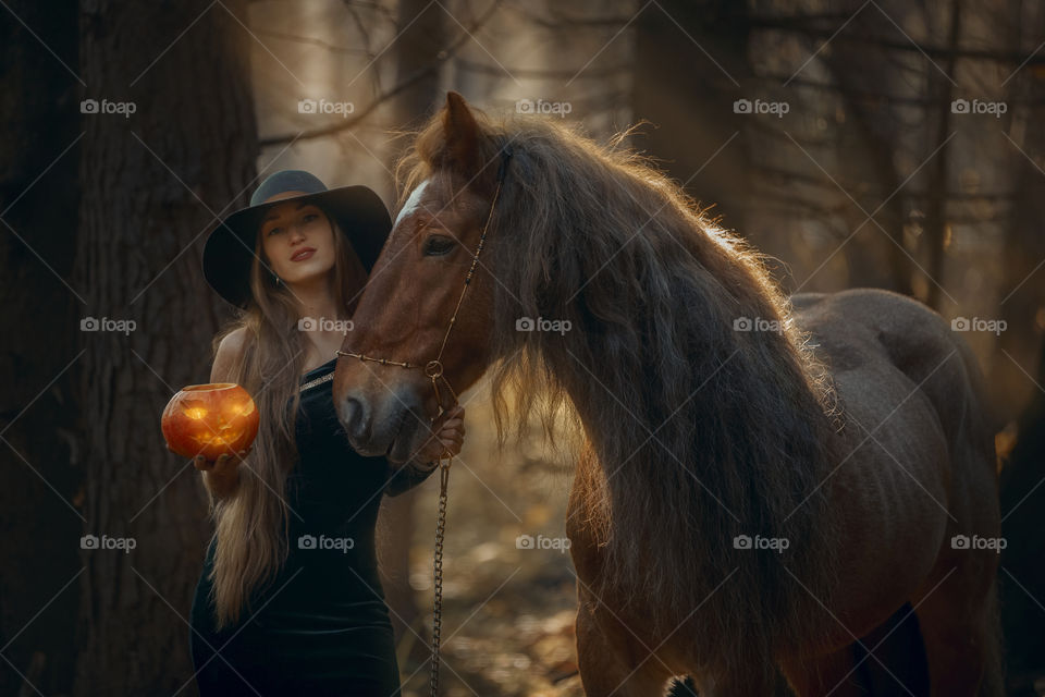 Woman in witch wear with horse in autumn park 