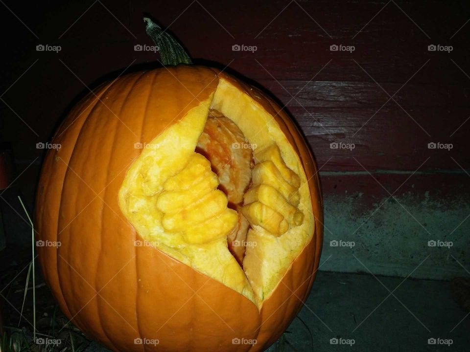Two hands splitting the wall of a pumpkin so that their owner can escape from inside.