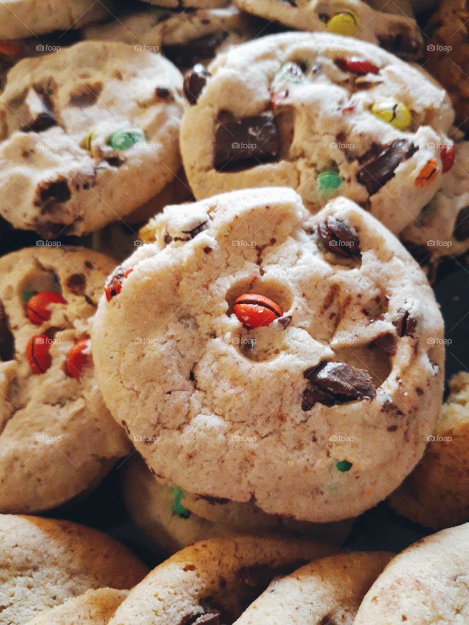 A bunch of delicious chocolate chip cookies with different colored candy coated chocolate pieces in them.