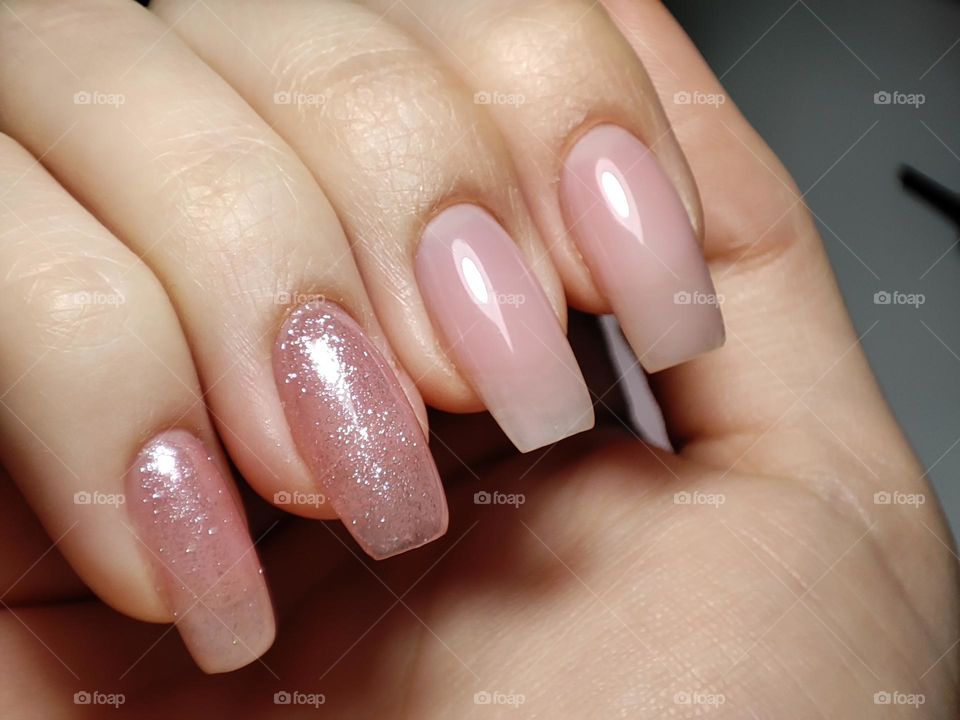 Gel nail manicure with pink glittery polish/ Beautiful polish on nails/ Naturally long nails with gel nail polish/Pink nails with a simple design up close in the light