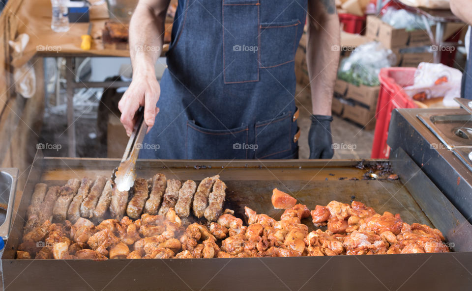 Cook's hands fries pork meat cutlets and burgers on a steaming grill. Barbeque cooking.