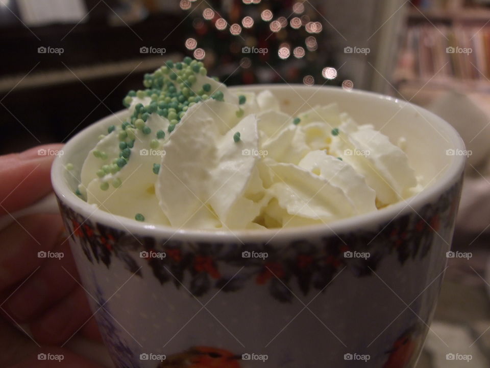 Hot chocolate and whipped cream in a closeup view with Christmas tree in the background
