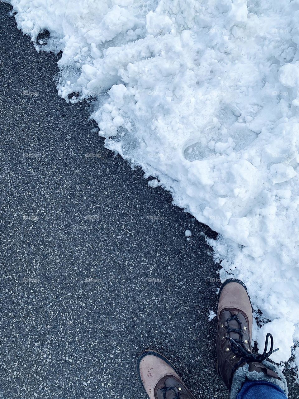 A person’s boots stand between the road and snow.