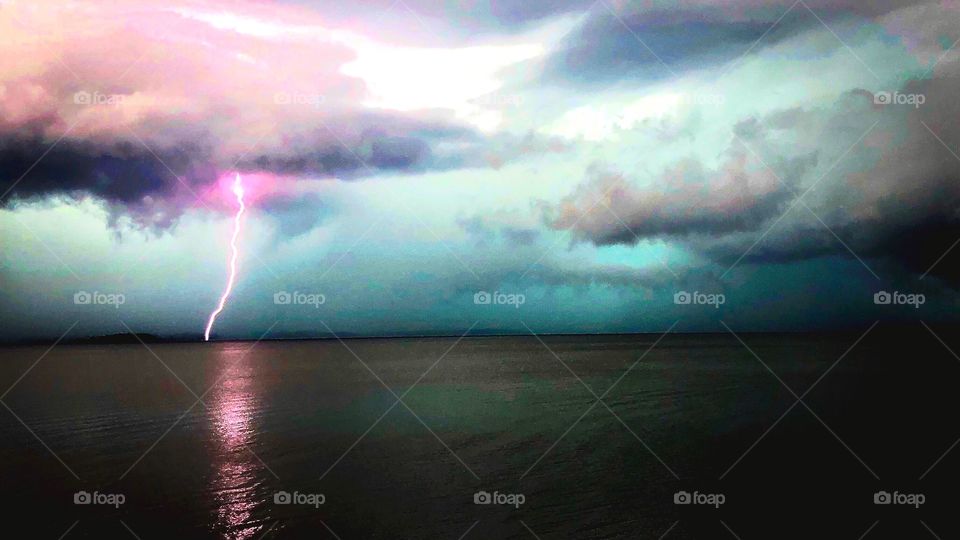 Lightning bolt over calm water. Cool, moody colors 