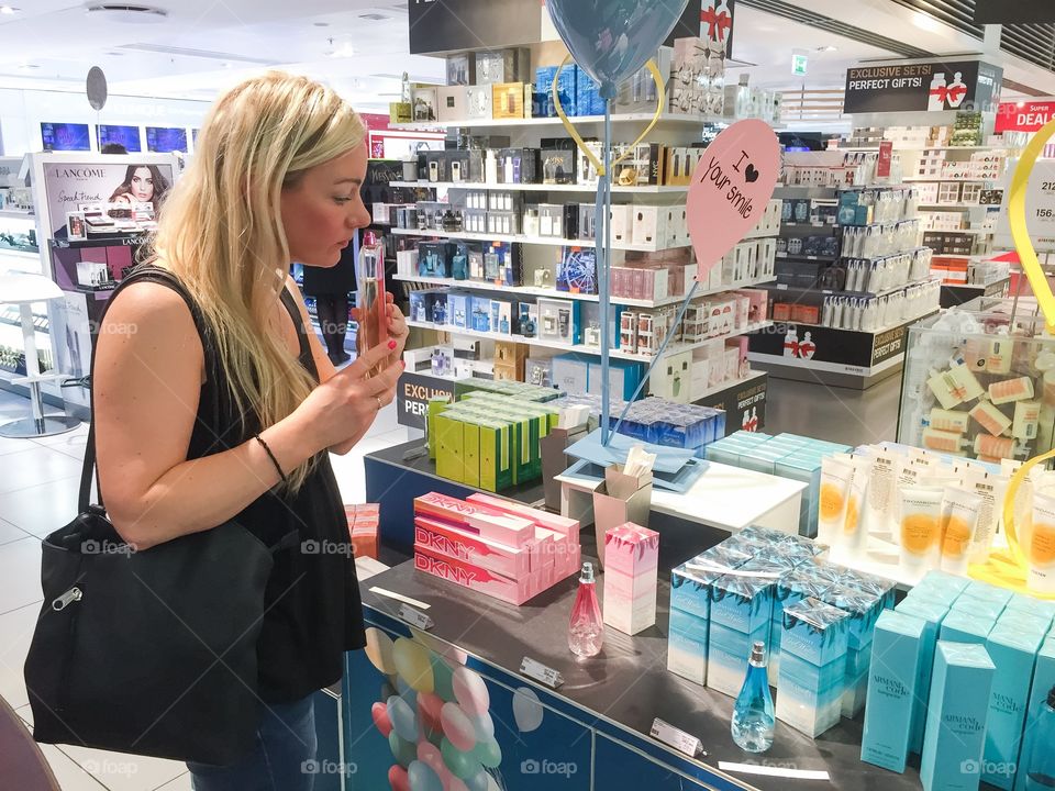 Young woman in her 30 years is smells perfume in a Taxfree shop at Copenhagen airport in Denmark.